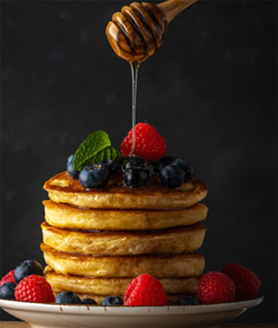 image of syrup being poured onto pancakes and fruits on a dish